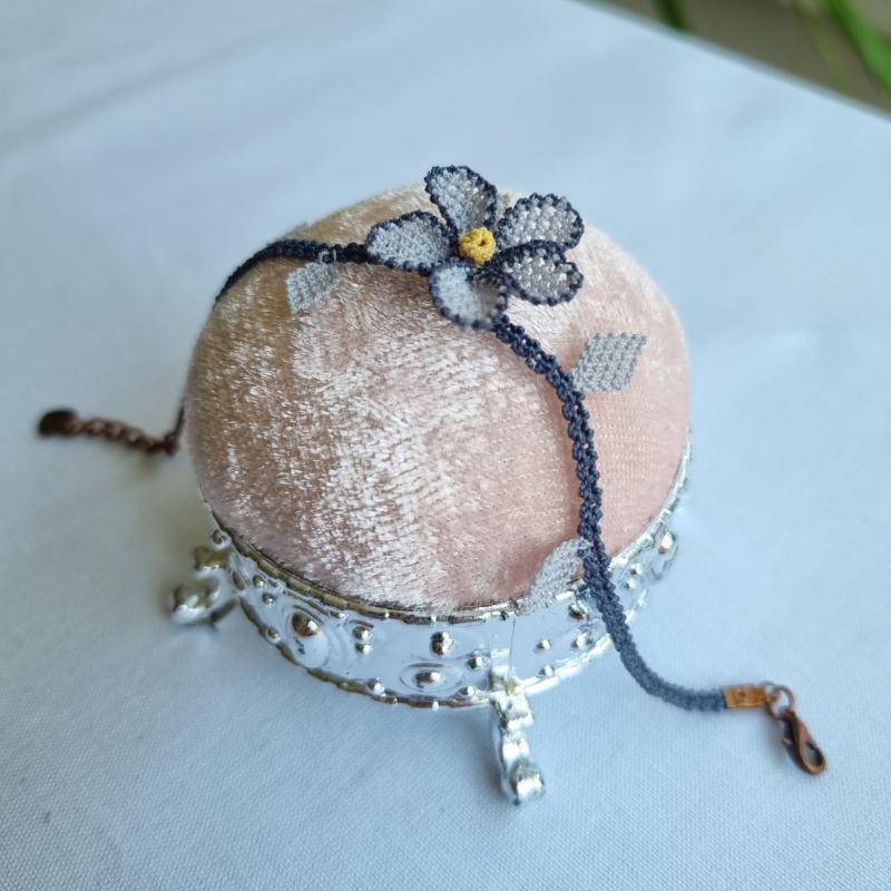 A handmade bracelet with a single gray needle lace flower, pale yellow center, and soft gray leaves on a gray band. Made from artificial silk thread using Turkish Oya technique.