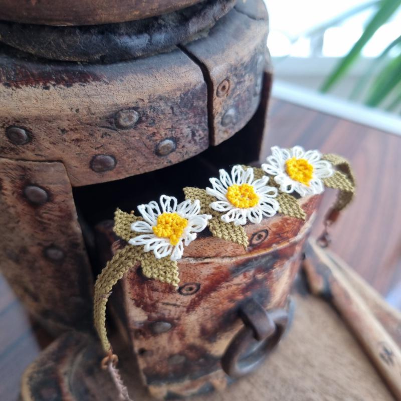 A handmade bracelet with three white daisy flowers made from needle lace, featuring yellow centers and green leaves, set on an olive green adjustable band. Made using artificial silk thread with traditional Turkish Oya technique.
