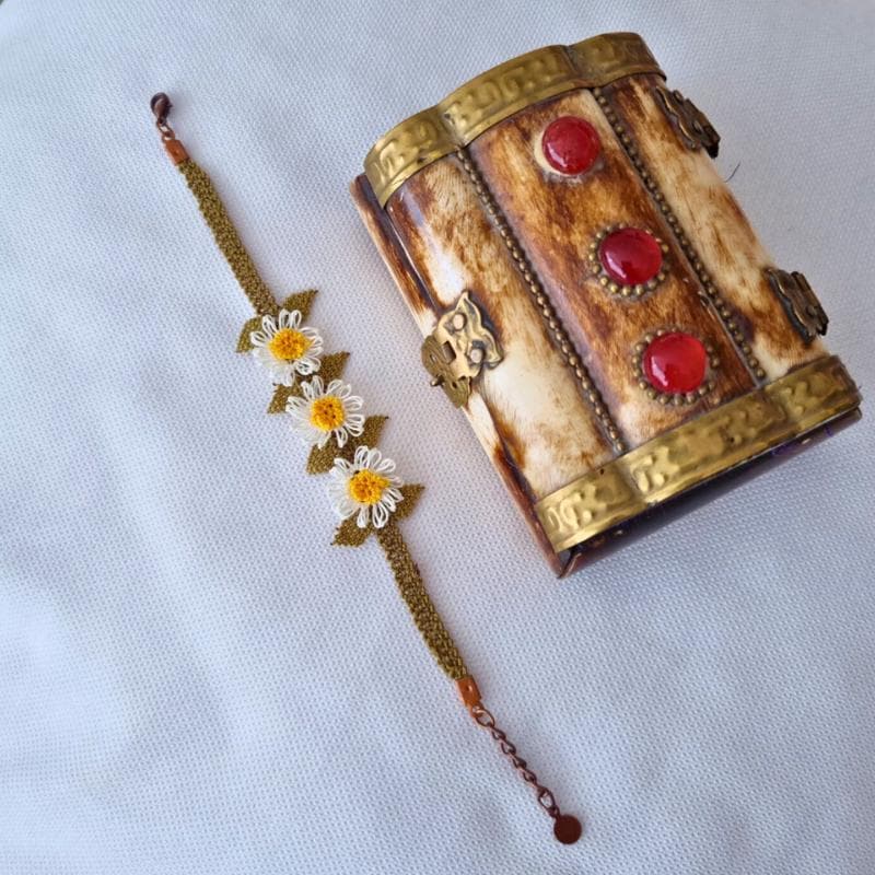 A handmade bracelet with three white daisy flowers made from needle lace, featuring yellow centers and green leaves, set on an olive green adjustable band. Made using artificial silk thread with traditional Turkish Oya technique.