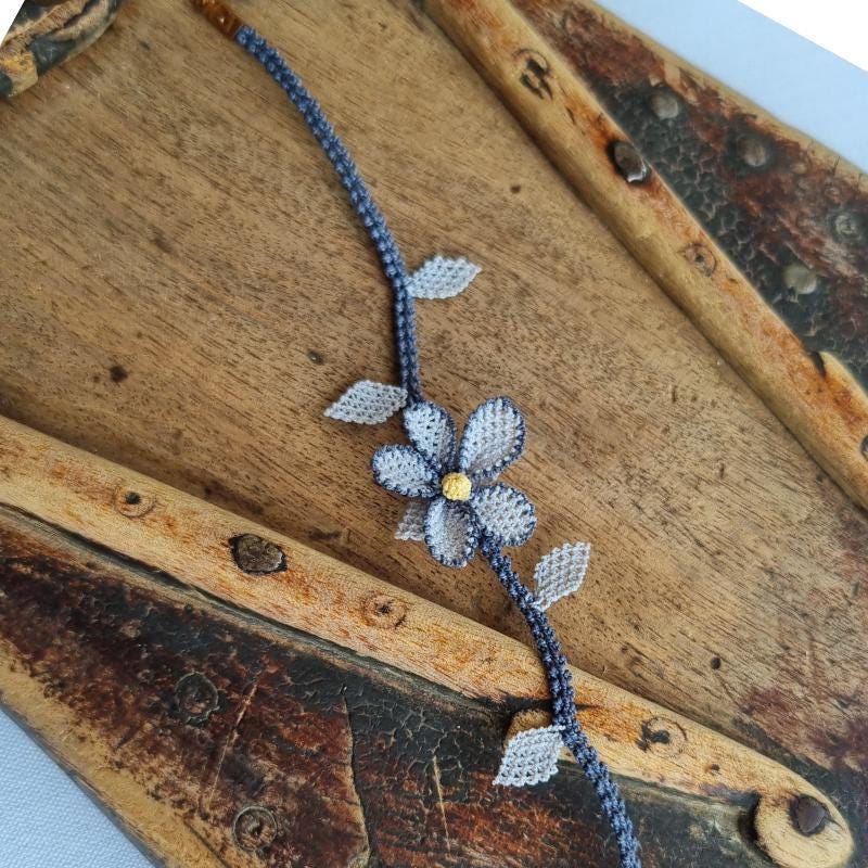 A handmade bracelet with a single gray needle lace flower, pale yellow center, and soft gray leaves on a gray band. Made from artificial silk thread using Turkish Oya technique.