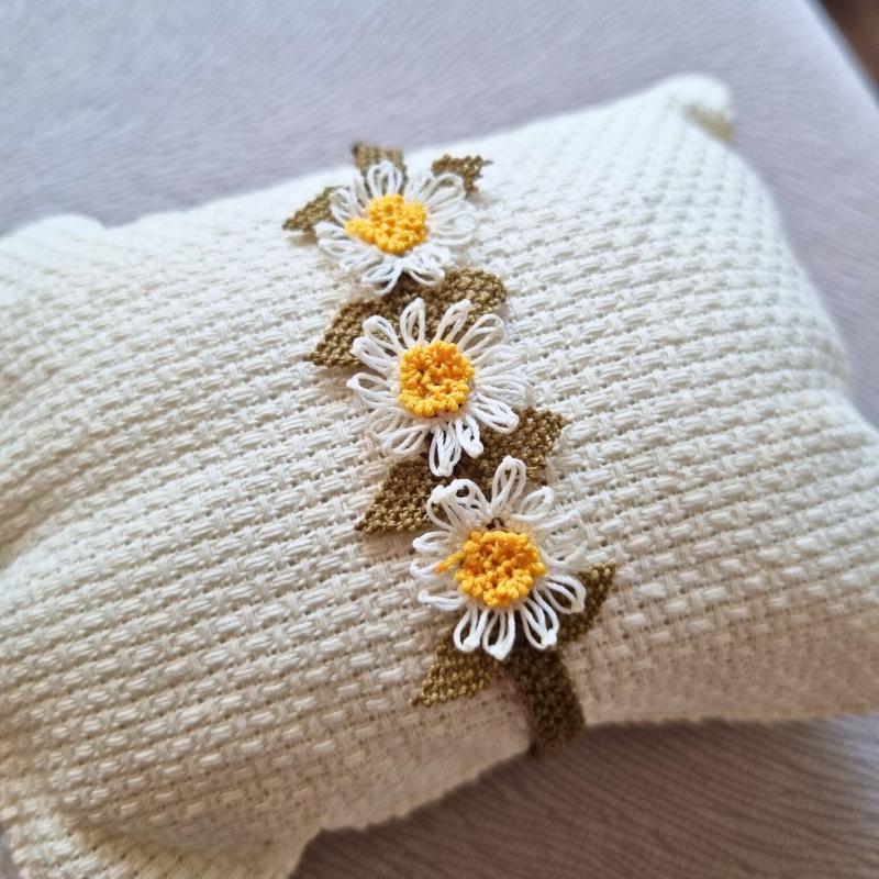A handmade bracelet with three white daisy flowers made from needle lace, featuring yellow centers and green leaves, set on an olive green adjustable band. Made using artificial silk thread with traditional Turkish Oya technique.
