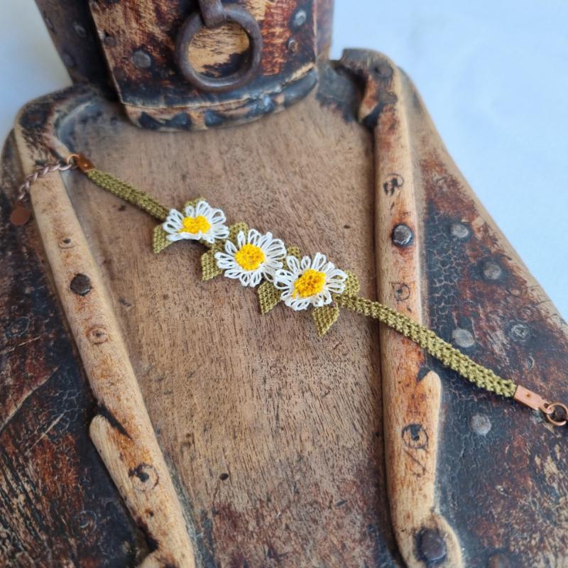 A handmade bracelet with three white daisy flowers made from needle lace, featuring yellow centers and green leaves, set on an olive green adjustable band. Made using artificial silk thread with traditional Turkish Oya technique.