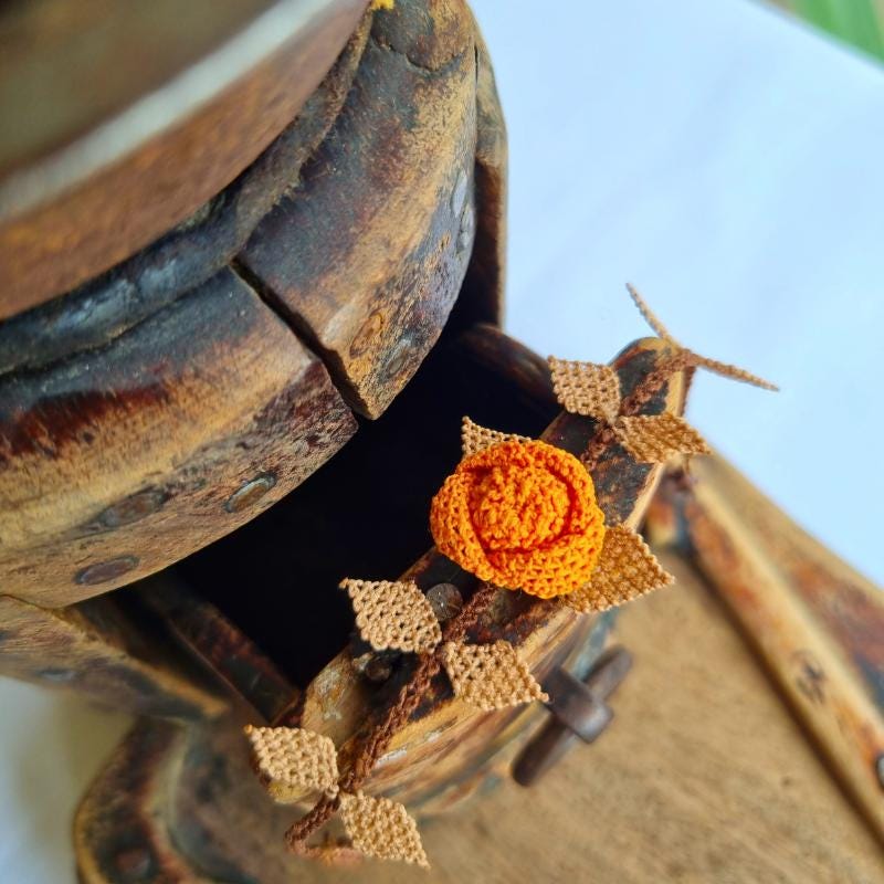 A handmade bracelet featuring a single orange rose with brown needle lace leaves on a brown band, made with artificial silk thread using the traditional Turkish Oya technique.