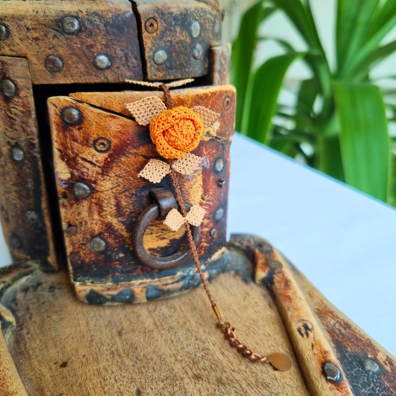 A handmade bracelet featuring a single orange rose with brown needle lace leaves on a brown band, made with artificial silk thread using the traditional Turkish Oya technique.