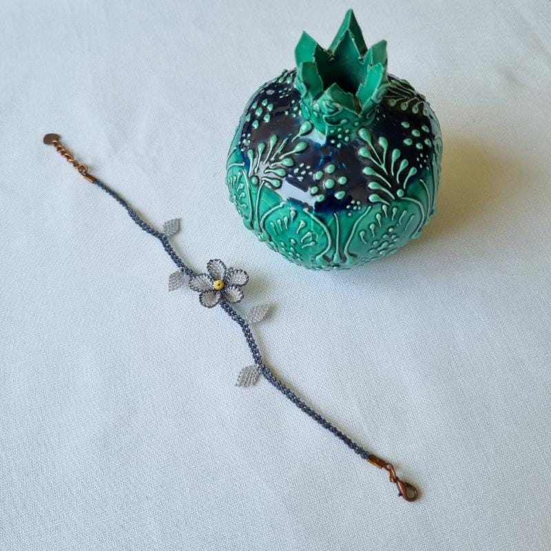 A handmade bracelet with a single gray needle lace flower, pale yellow center, and soft gray leaves on a gray band. Made from artificial silk thread using Turkish Oya technique.