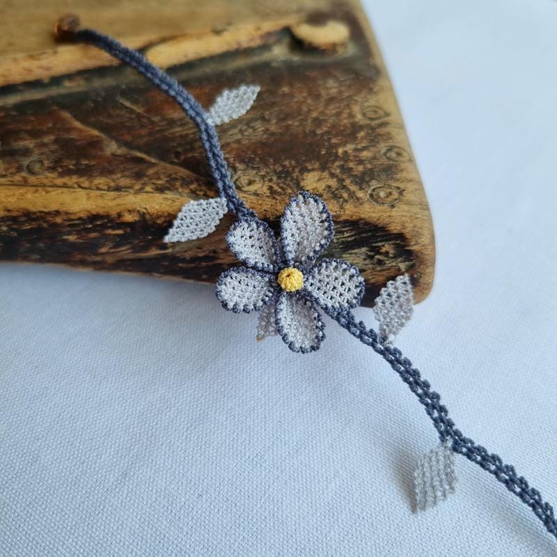 A handmade bracelet with a single gray needle lace flower, pale yellow center, and soft gray leaves on a gray band. Made from artificial silk thread using Turkish Oya technique.